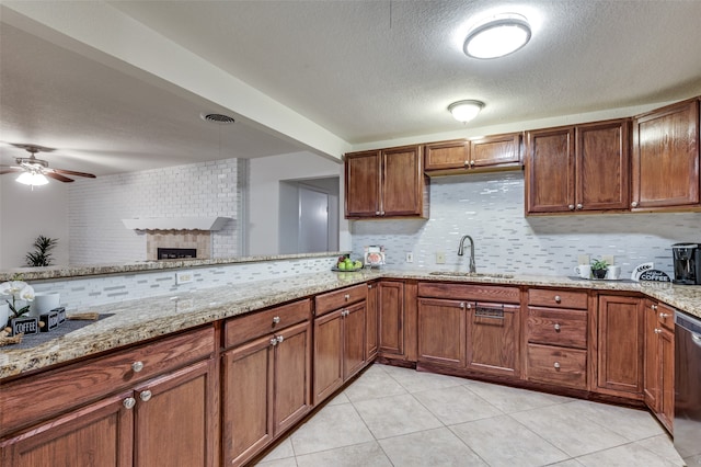 kitchen with sink, stainless steel dishwasher, a fireplace, tasteful backsplash, and light stone counters