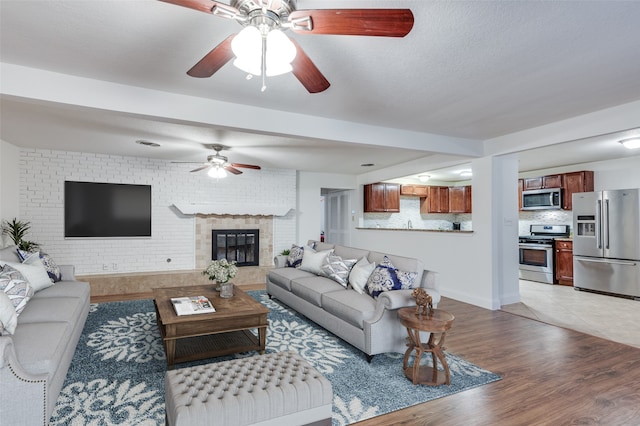 living room featuring ceiling fan, light hardwood / wood-style floors, and a brick fireplace