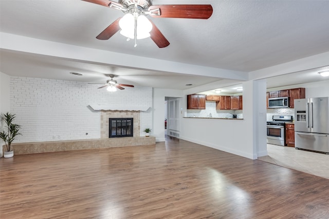 unfurnished living room featuring a fireplace, light hardwood / wood-style flooring, ceiling fan, and brick wall