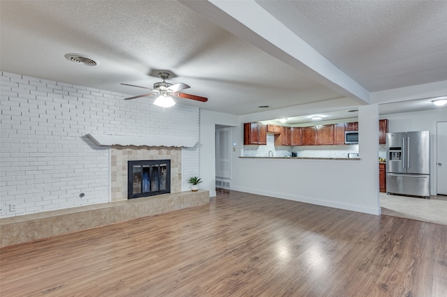 unfurnished living room with a textured ceiling, ceiling fan, wood-type flooring, and a fireplace