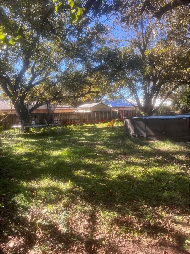 view of yard with a trampoline and a covered pool