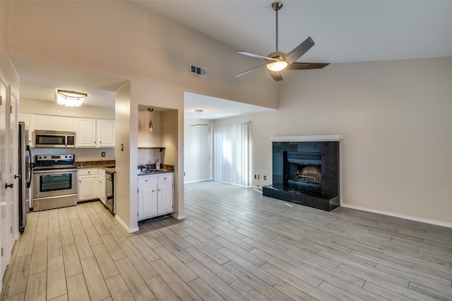 kitchen with white cabinetry, a high end fireplace, light wood-type flooring, and appliances with stainless steel finishes