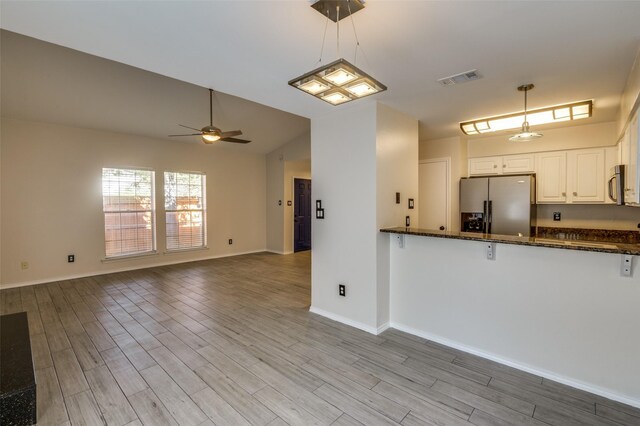 kitchen with appliances with stainless steel finishes, light wood-type flooring, dark stone counters, decorative light fixtures, and white cabinets