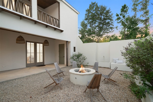 patio terrace at dusk featuring a balcony, an outdoor fire pit, and french doors