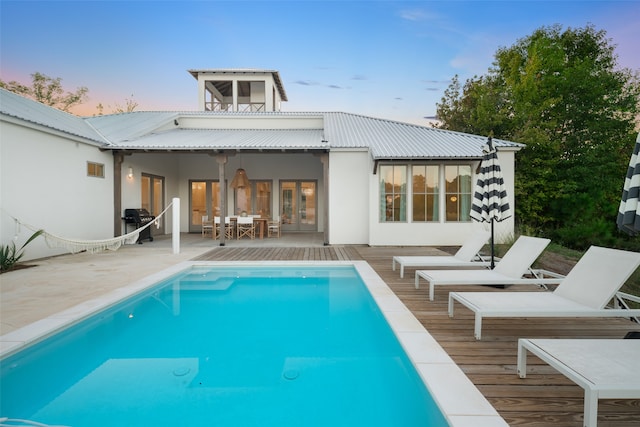 back house at dusk with a pool side deck and french doors