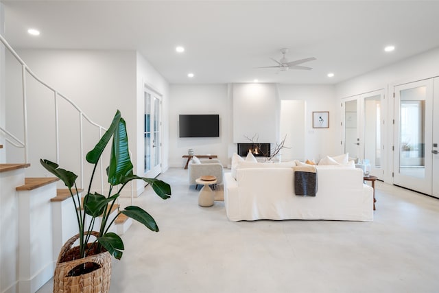 living room featuring ceiling fan, a large fireplace, and french doors