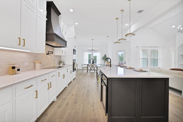 kitchen featuring a large island with sink, white cabinets, light hardwood / wood-style flooring, decorative light fixtures, and custom range hood