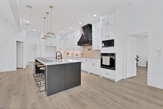 kitchen featuring premium range hood, oven, white cabinetry, and an island with sink