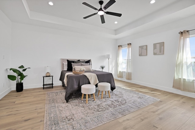 bedroom with light hardwood / wood-style floors, a raised ceiling, and ceiling fan