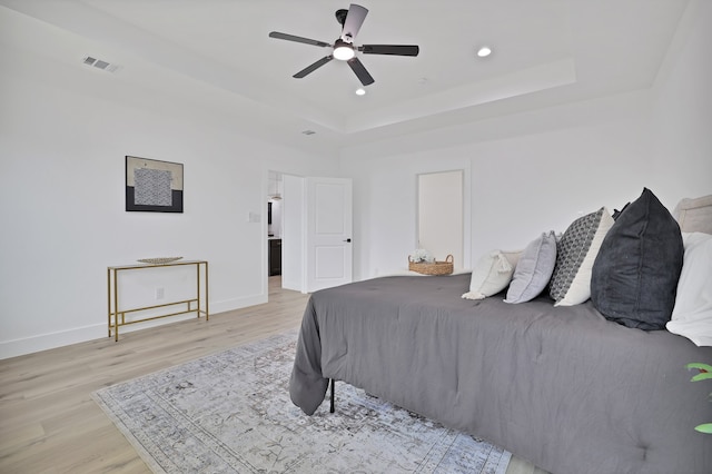 bedroom featuring light wood-type flooring, a raised ceiling, and ceiling fan