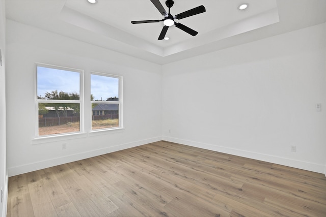 unfurnished room with a raised ceiling, ceiling fan, and light hardwood / wood-style floors