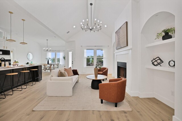 living room with a chandelier, light wood-type flooring, high vaulted ceiling, and sink