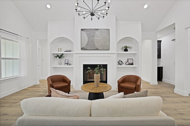 living room with built in shelves, lofted ceiling, a chandelier, and light hardwood / wood-style flooring