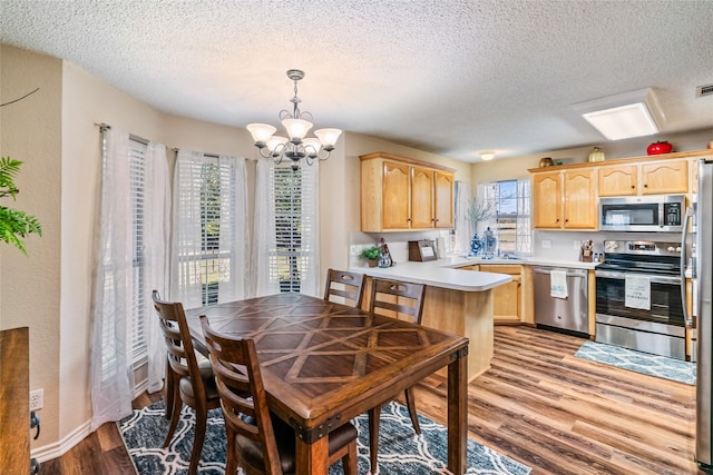 kitchen featuring a textured ceiling, stainless steel appliances, pendant lighting, light brown cabinets, and light hardwood / wood-style flooring