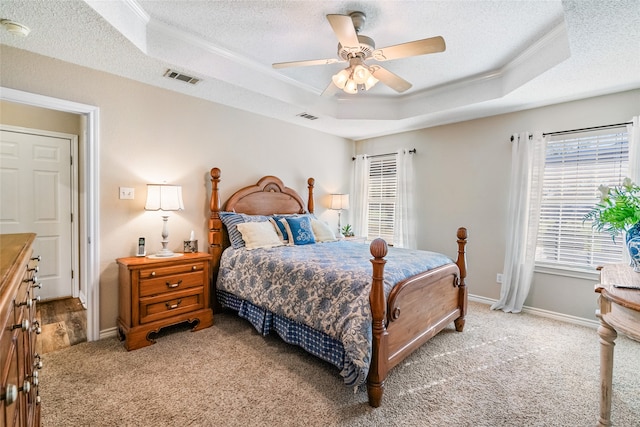 bedroom featuring light carpet, a textured ceiling, a tray ceiling, ceiling fan, and crown molding