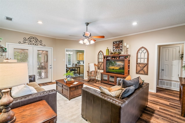 living room featuring ceiling fan, light hardwood / wood-style floors, ornamental molding, and a textured ceiling