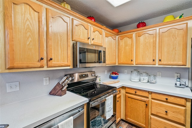 kitchen with wood-type flooring, a textured ceiling, stainless steel appliances, and light brown cabinets