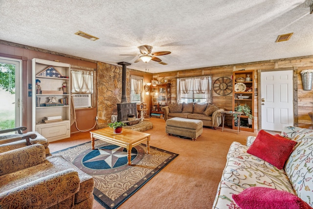 carpeted living room featuring a wood stove, ceiling fan, and a textured ceiling