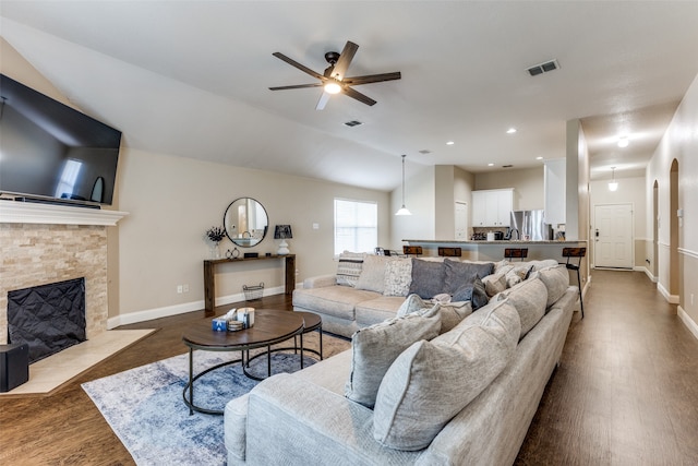 living room with ceiling fan, a stone fireplace, wood-type flooring, and vaulted ceiling