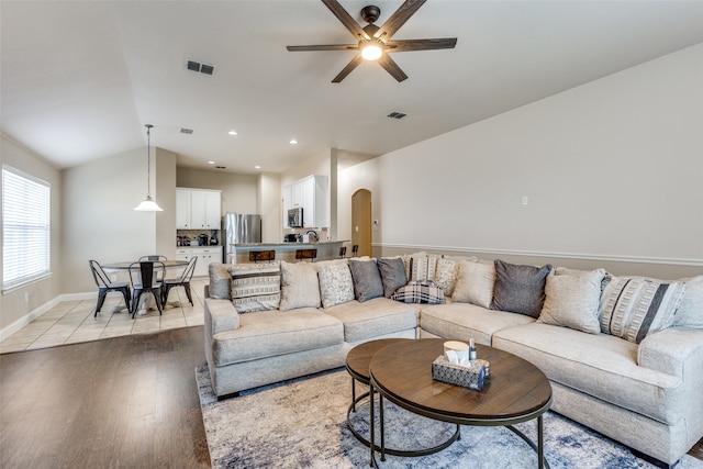 living room with ceiling fan, vaulted ceiling, and light wood-type flooring