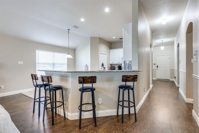 kitchen featuring light stone countertops, dark hardwood / wood-style flooring, a breakfast bar, white cabinetry, and hanging light fixtures