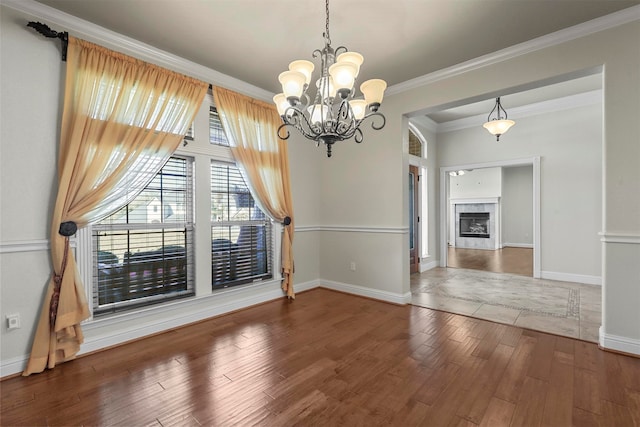 unfurnished dining area with hardwood / wood-style flooring, crown molding, an inviting chandelier, and a tile fireplace