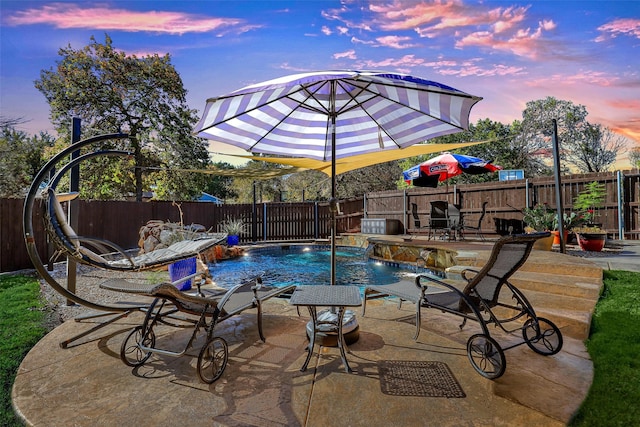 pool at dusk with pool water feature and a patio area