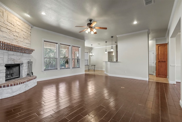 unfurnished living room featuring dark wood-type flooring, ornamental molding, a stone fireplace, and ceiling fan with notable chandelier