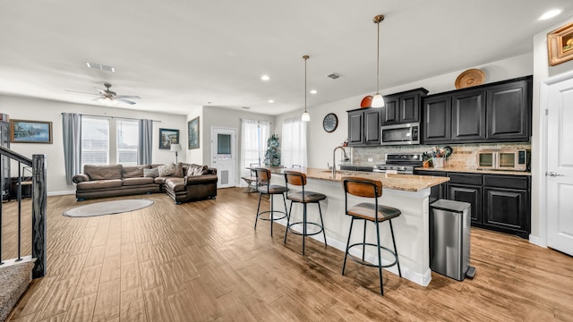 kitchen with stainless steel appliances, light stone counters, light hardwood / wood-style floors, a kitchen island with sink, and a breakfast bar