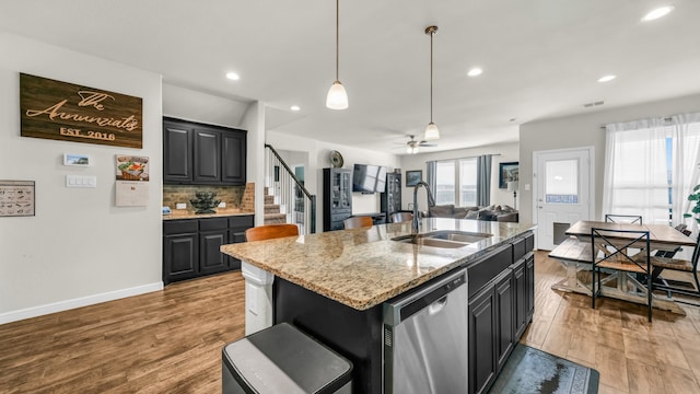 kitchen with a kitchen bar, stainless steel dishwasher, sink, a center island with sink, and light hardwood / wood-style floors