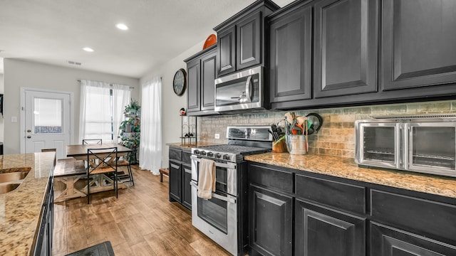 kitchen featuring light stone countertops, backsplash, stainless steel appliances, and light hardwood / wood-style flooring