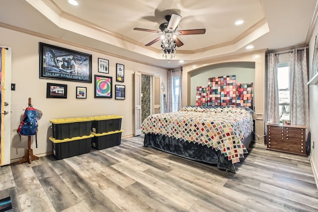 bedroom with wood-type flooring, a tray ceiling, ceiling fan, and ornamental molding