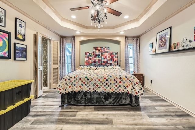 bedroom featuring hardwood / wood-style floors, ceiling fan, ornamental molding, and a tray ceiling