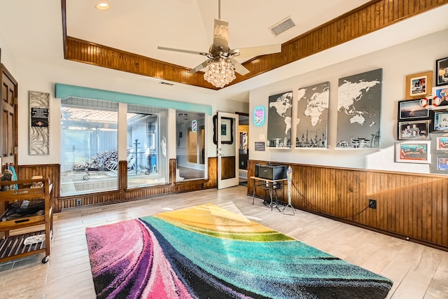 interior space featuring ceiling fan, a towering ceiling, wooden walls, and light hardwood / wood-style flooring