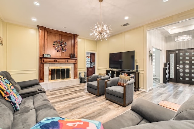 living room featuring a chandelier, light wood-type flooring, a tile fireplace, and crown molding