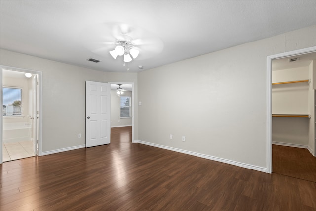 unfurnished bedroom featuring a spacious closet, a closet, ceiling fan, and dark hardwood / wood-style floors