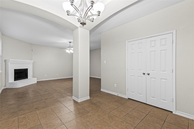 unfurnished living room with tile patterned floors, an inviting chandelier, and a brick fireplace