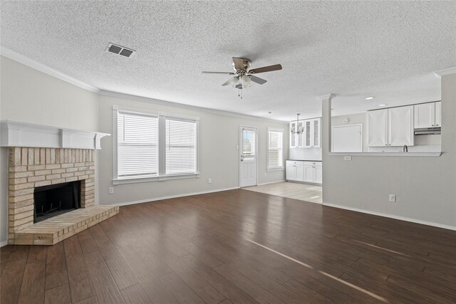 unfurnished living room featuring crown molding, light wood-type flooring, a textured ceiling, and a brick fireplace