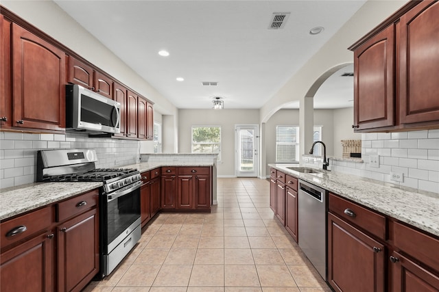 kitchen featuring sink, decorative backsplash, light stone countertops, appliances with stainless steel finishes, and kitchen peninsula