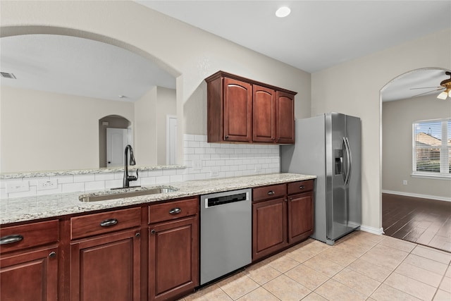 kitchen featuring sink, light stone counters, backsplash, appliances with stainless steel finishes, and light wood-type flooring