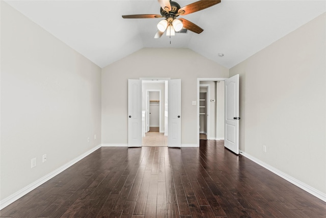 unfurnished bedroom featuring a walk in closet, vaulted ceiling, ceiling fan, and dark wood-type flooring