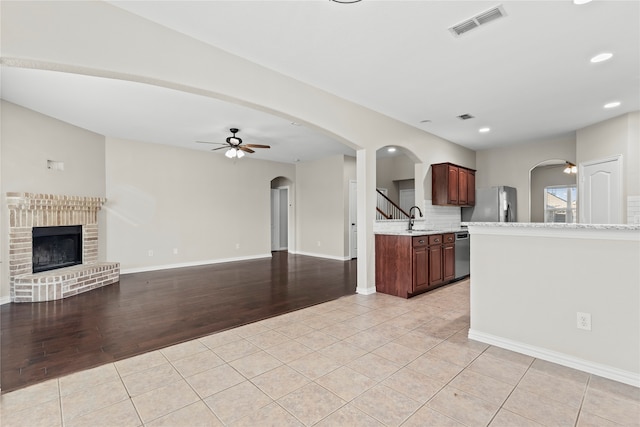 kitchen featuring dishwasher, a brick fireplace, ceiling fan, tasteful backsplash, and light hardwood / wood-style floors