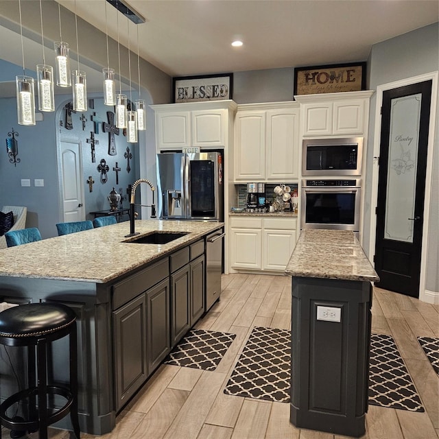 kitchen featuring light stone countertops, white cabinets, appliances with stainless steel finishes, sink, and a kitchen island with sink