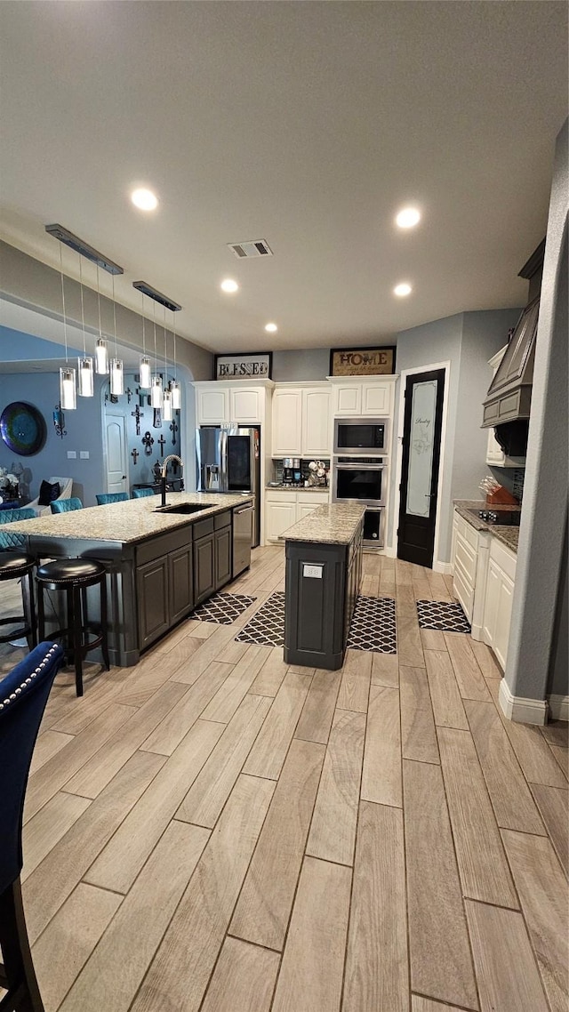 kitchen with decorative light fixtures, white cabinetry, stainless steel appliances, sink, and a center island with sink