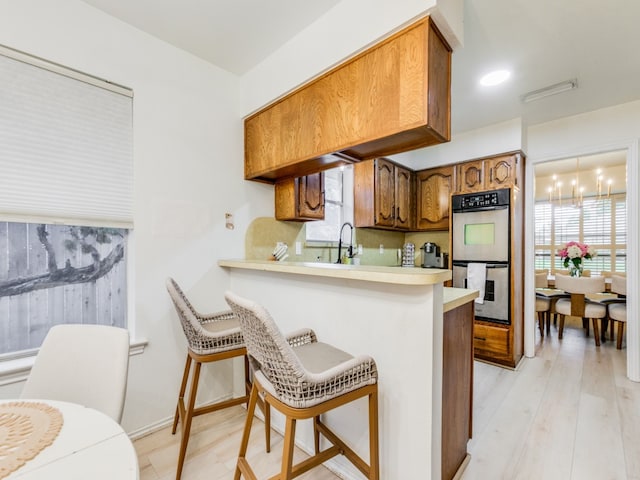 kitchen with double oven, a wealth of natural light, a kitchen bar, and light wood-type flooring