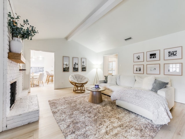 bedroom with a brick fireplace, vaulted ceiling with beams, and light hardwood / wood-style flooring