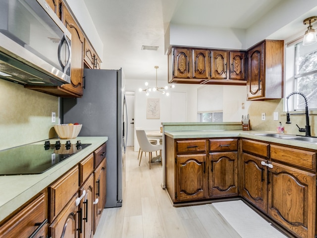 kitchen with an inviting chandelier, sink, light wood-type flooring, black electric cooktop, and decorative light fixtures