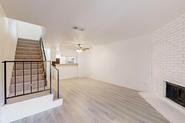 unfurnished living room with ceiling fan, wood-type flooring, and a brick fireplace