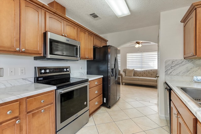 kitchen featuring light tile patterned floors, a textured ceiling, stainless steel appliances, and ceiling fan