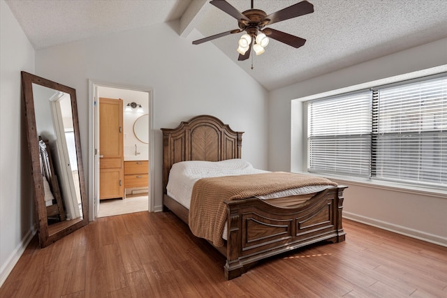 bedroom with connected bathroom, ceiling fan, vaulted ceiling with beams, wood-type flooring, and a textured ceiling